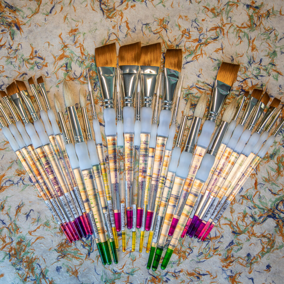 A variety of paint brushes are fanned out on a table