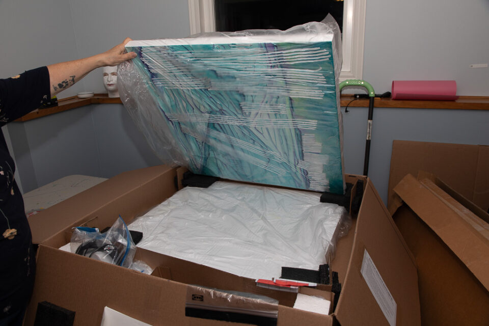 The artist holds a painting being packed with its tactile replica